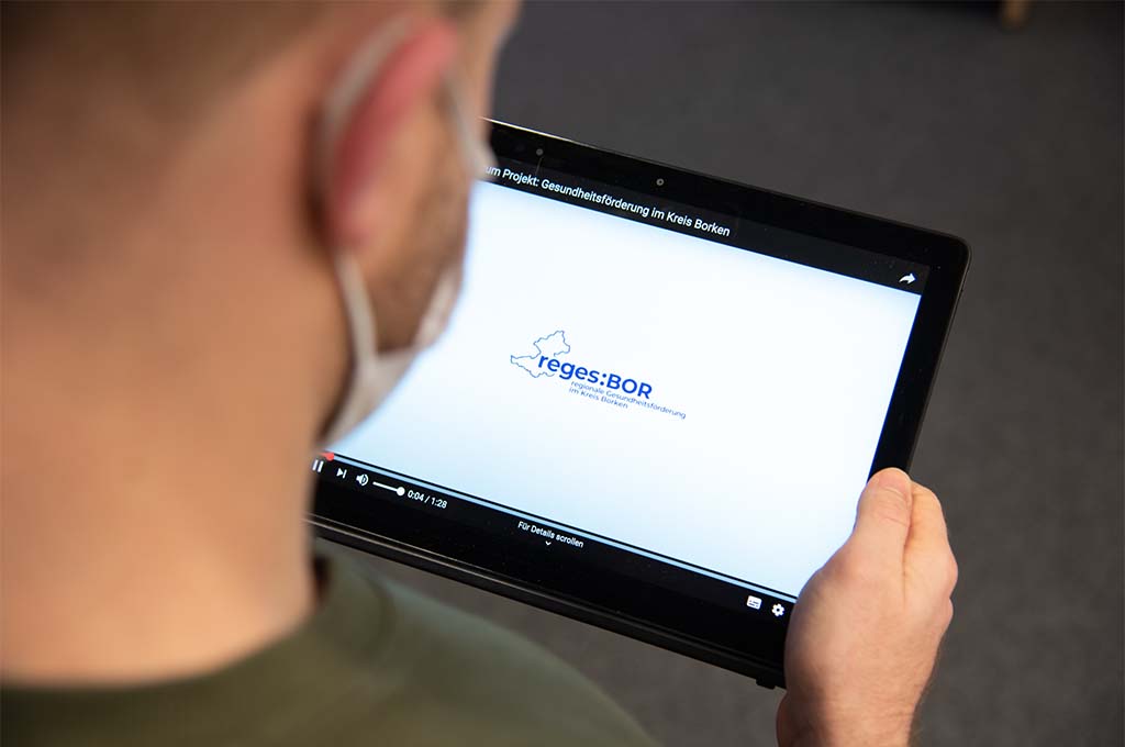 Mann hält ein Tablet in der Hand, auf dem das Logo des Projektes "reges:BOR" abgebildet ist.