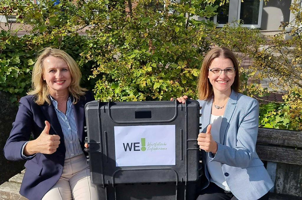 Die Professorinnen Julia Frohne (l.) und Kerstin Ettl (r.) sitzen auf einer Bank und halten gemeinsam einen „Erfinderinnen-Werkzeugkoffer“ in der Hand